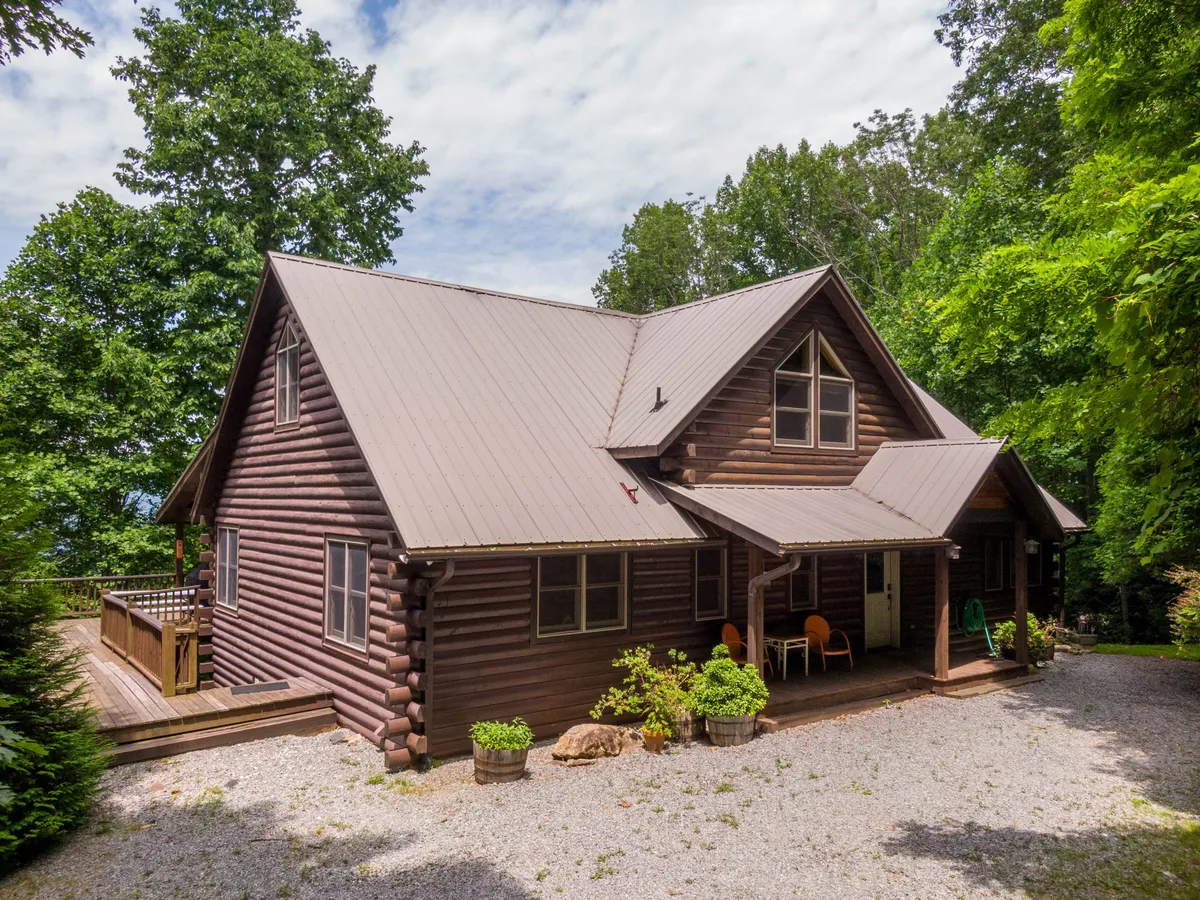 An exterior view of a log cabin with a welcoming front porch surrounded by lush greenery. The cozy scene suggests outdoor leisure, with the cabin nestled into its natural setting and inviting guests to step outside and enjoy the landscape.