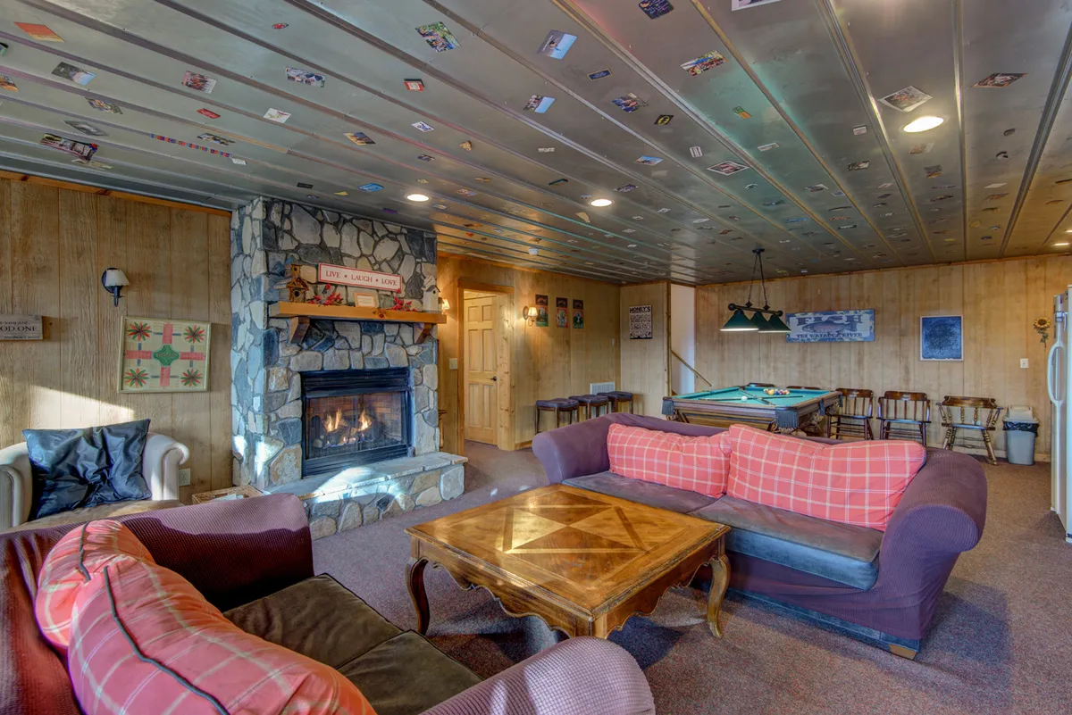 A warmly lit lounge showcases a fireplace, pool table, and comfortable sofas around a coffee table. The setup suggests a space for both socializing and relaxing, with ample room for guests and multiple entertainment options visible.