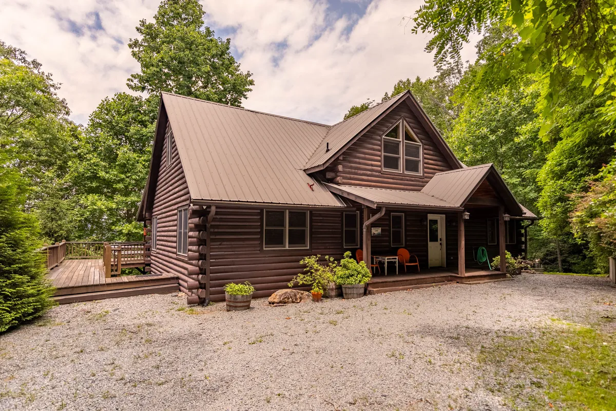 The image features the inviting log cabin facade of Four Points, with colorful chairs on the porch and decorative plants framing the entrance—all set in a lush natural environment.