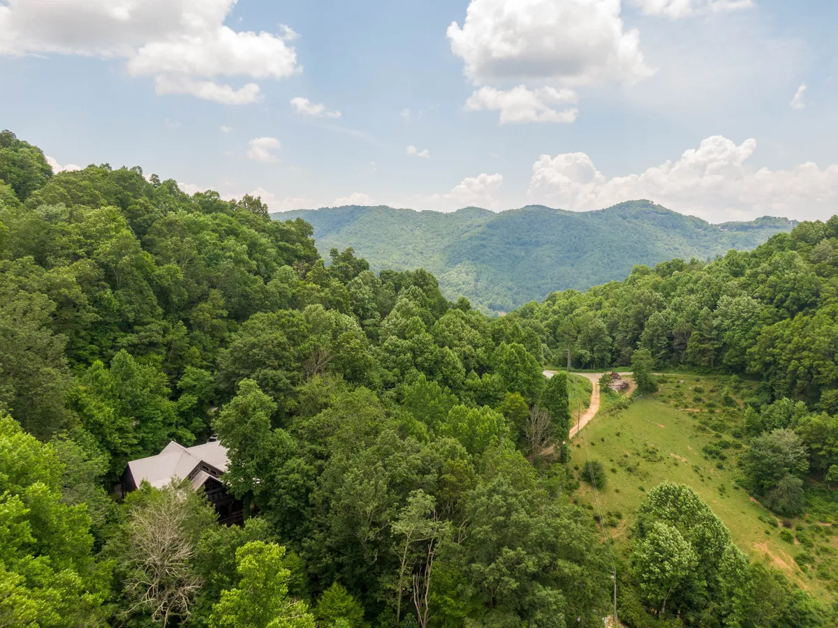 A breathtaking view of a mountain range covered in dense greenery, with a winding road leading through the landscape. A cozy cabin is nestled among the trees, emphasizing both seclusion and accessibility to nature. The image evokes a sense of adventure and serenity, capturing the core of a mountain retreat experience.