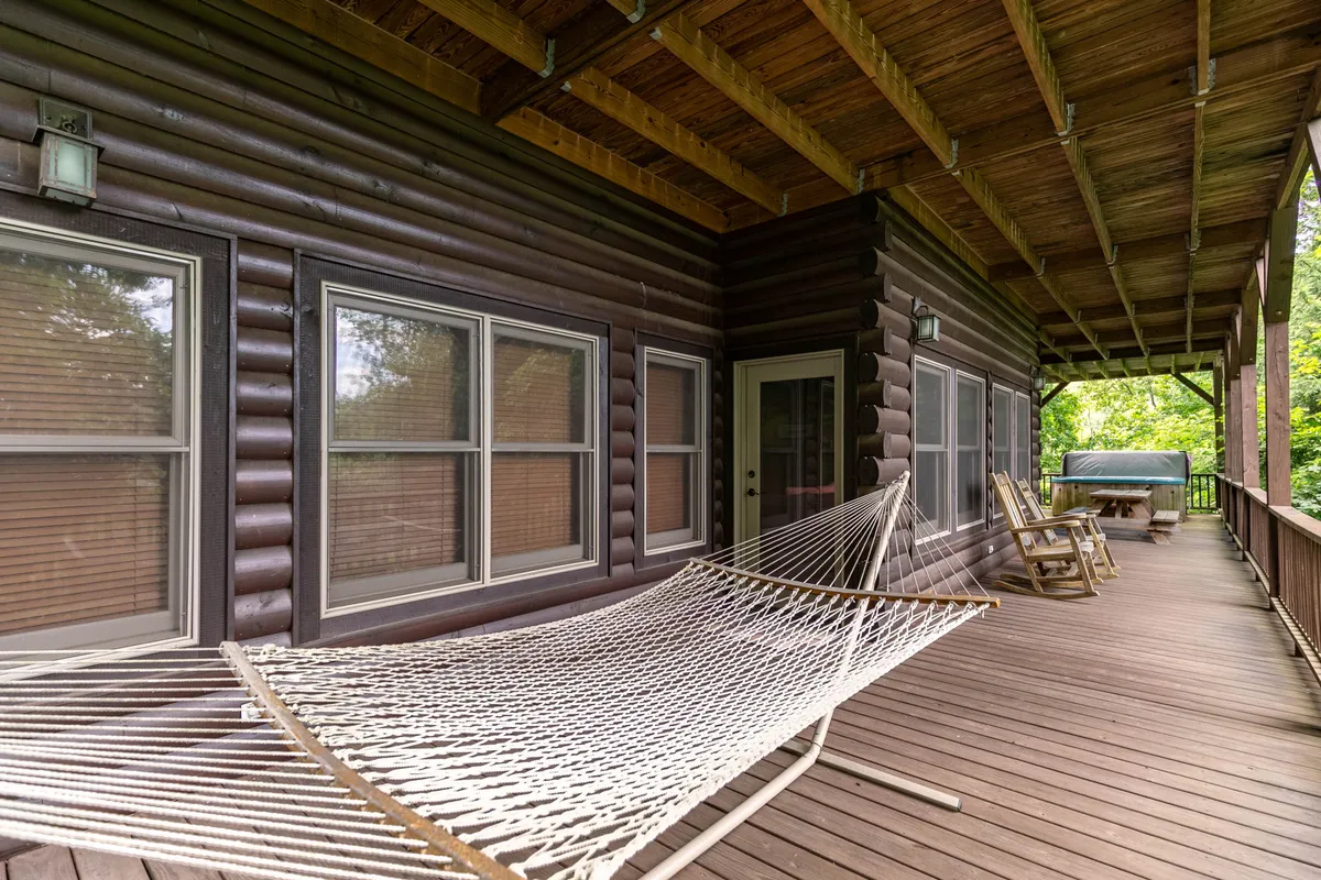 An inviting outdoor deck with a hammock, wooden railing, deck chairs, and large windows that connect the interior and exterior spaces. The area is set up for both relaxation and social activity with scenic natural views.