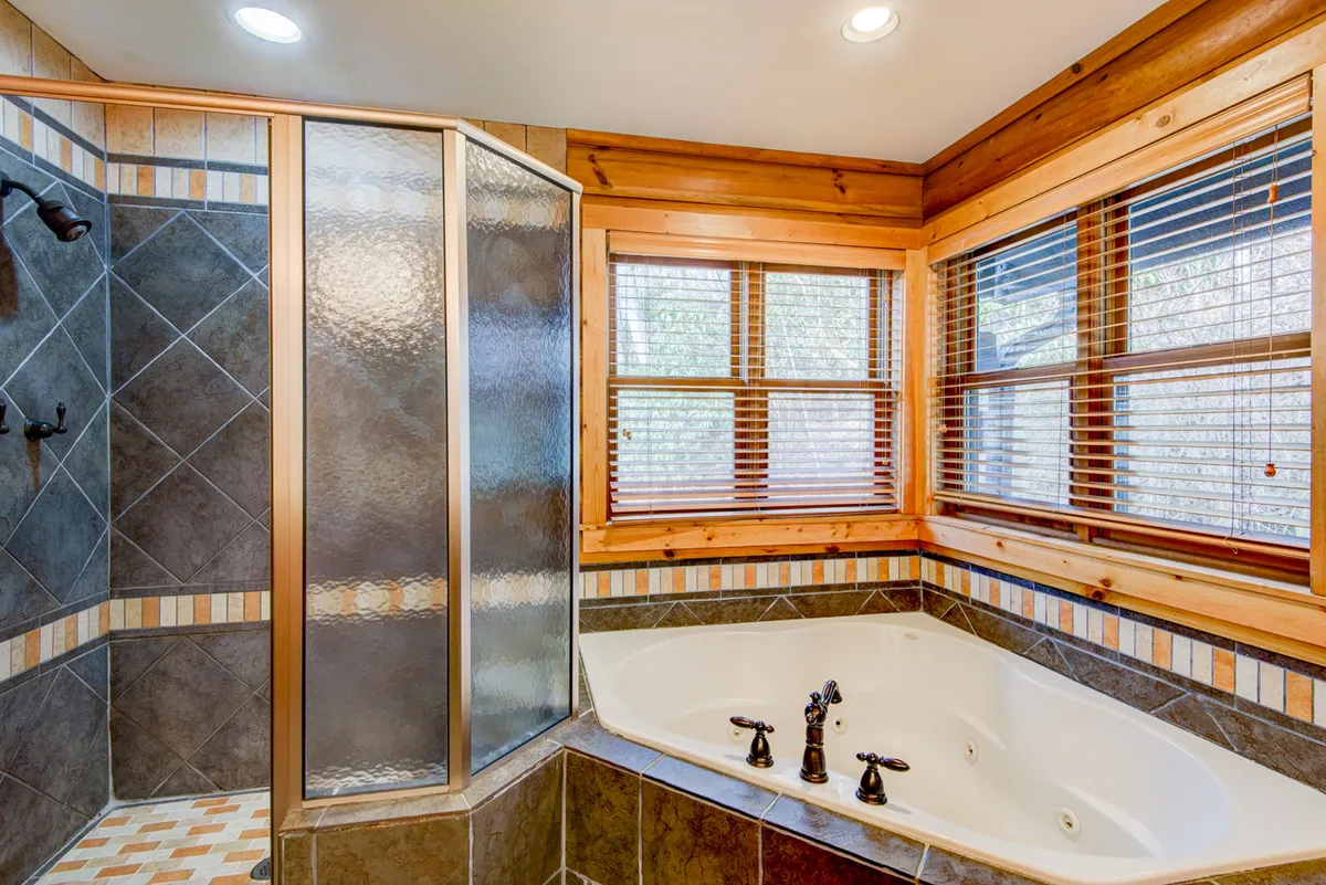 A tranquil bathroom scene with a large jacuzzi tub, separate shower enclosure, and rustic wooden window frames. Natural light fills the room, enhancing the spa-like, rejuvenating feel.